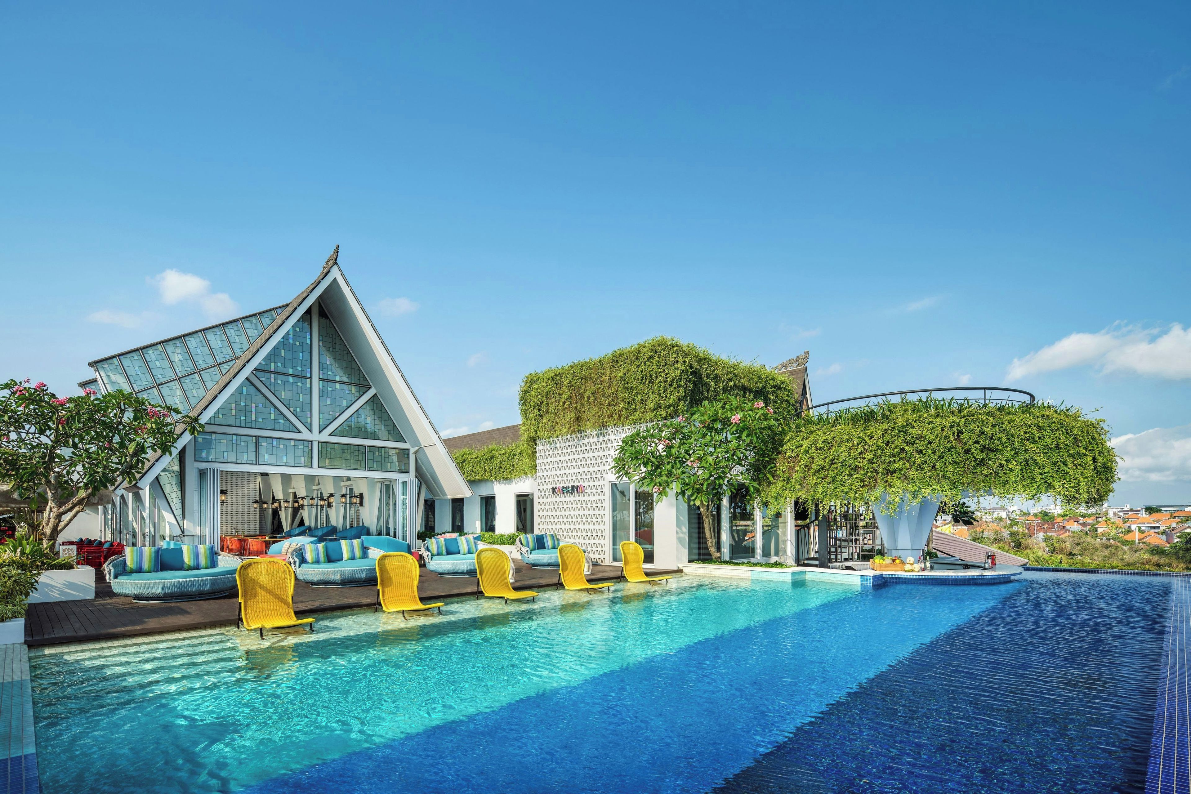 A modern hotel with a swimming pool, outdoor seating, and a unique triangular building.