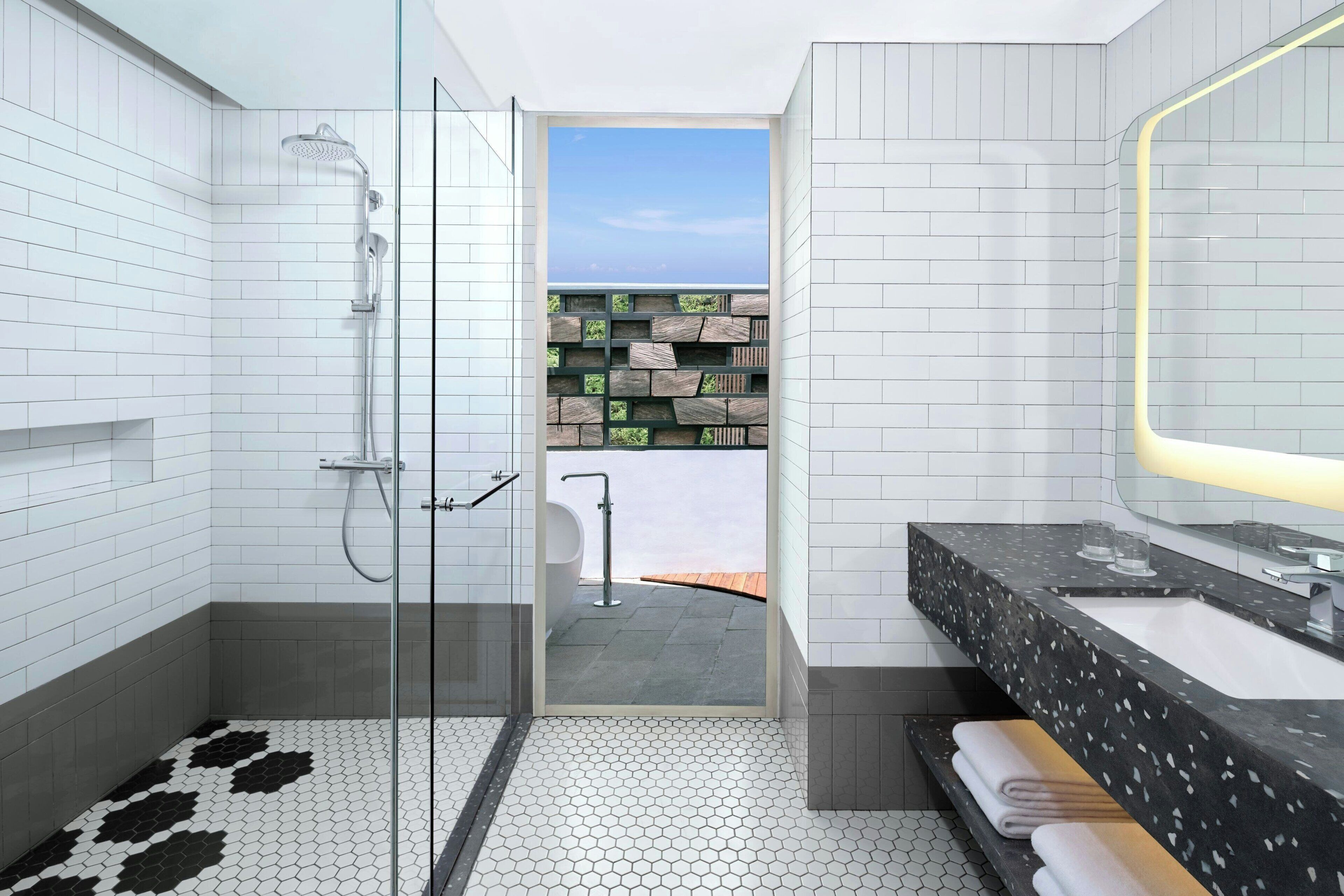 Une salle de bain moderne avec une douche à parois de verre, un grand miroir et une vue sur une terrasse en bois.