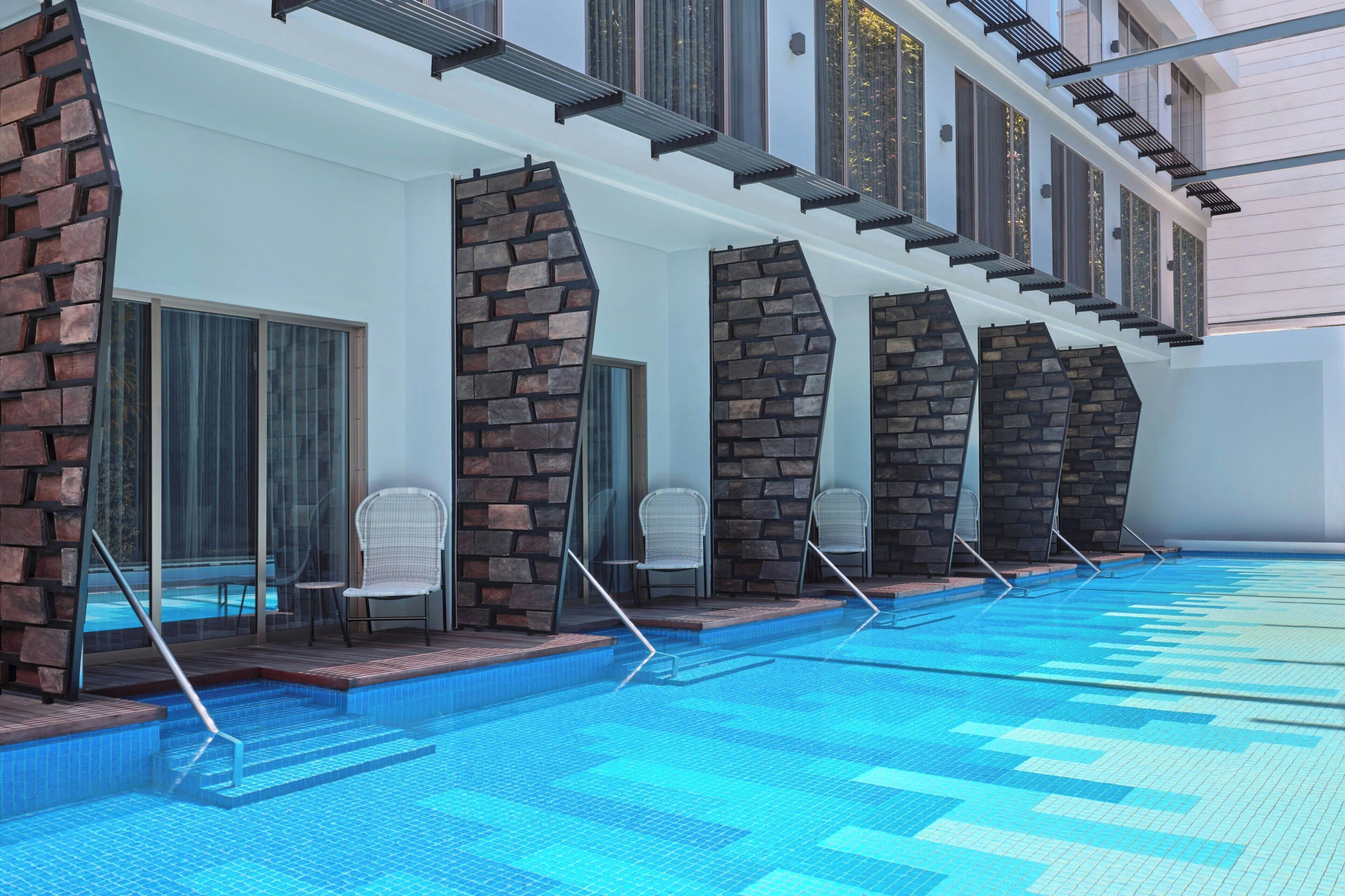 A swimming pool area with a modern design, featuring a series of stone pillars and glass doors leading to seating areas.