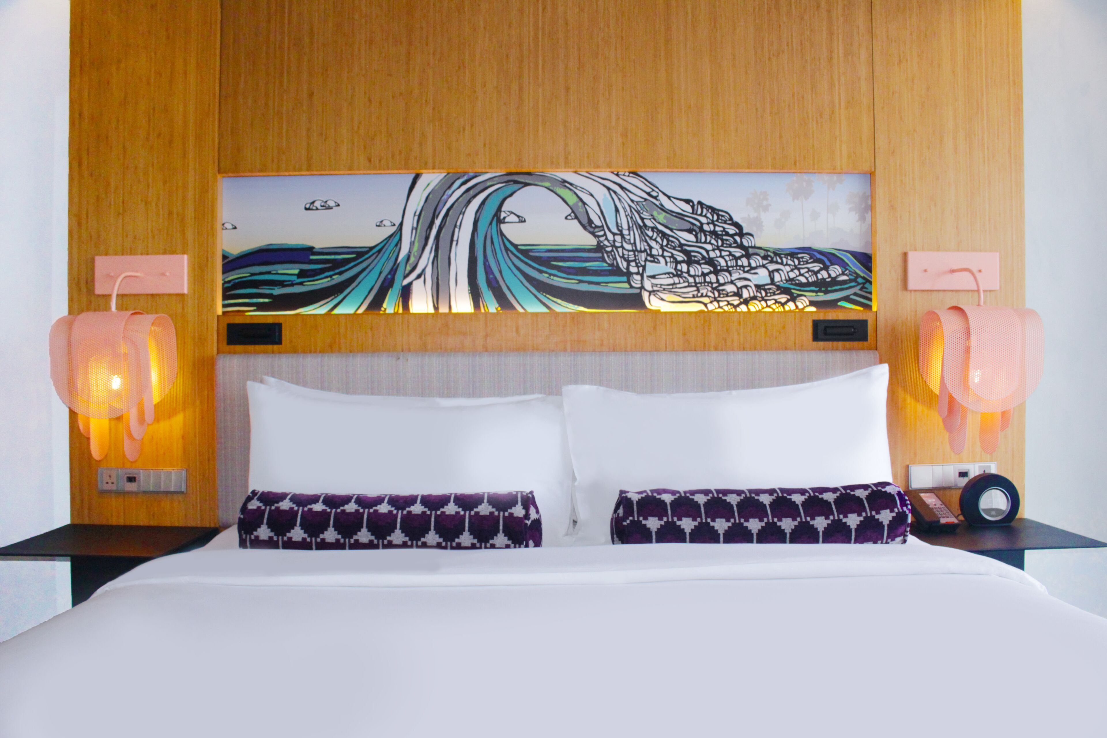 A hotel room with a bed, two pillows, a wall-mounted painting, and two bedside lamps.