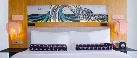 A hotel room with a bed, two pillows, a wall-mounted painting, and two bedside lamps.