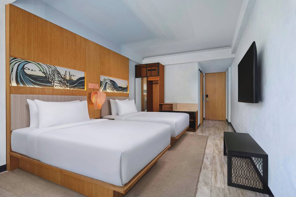 A hotel room with two beds, a wooden headboard, artwork, a TV, and a desk.