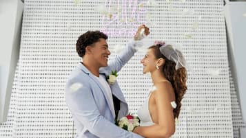 Una pareja vestida de novios con un letrero de neón y una pared con diseño de fondo.