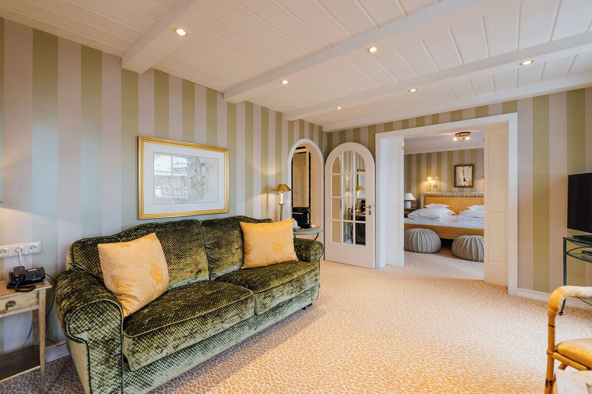 A room with a patterned sofa, a framed picture, and a bed with pillows.