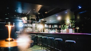 Zona de bar con taburetes y barra, con un letrero de neón y varias botellas.