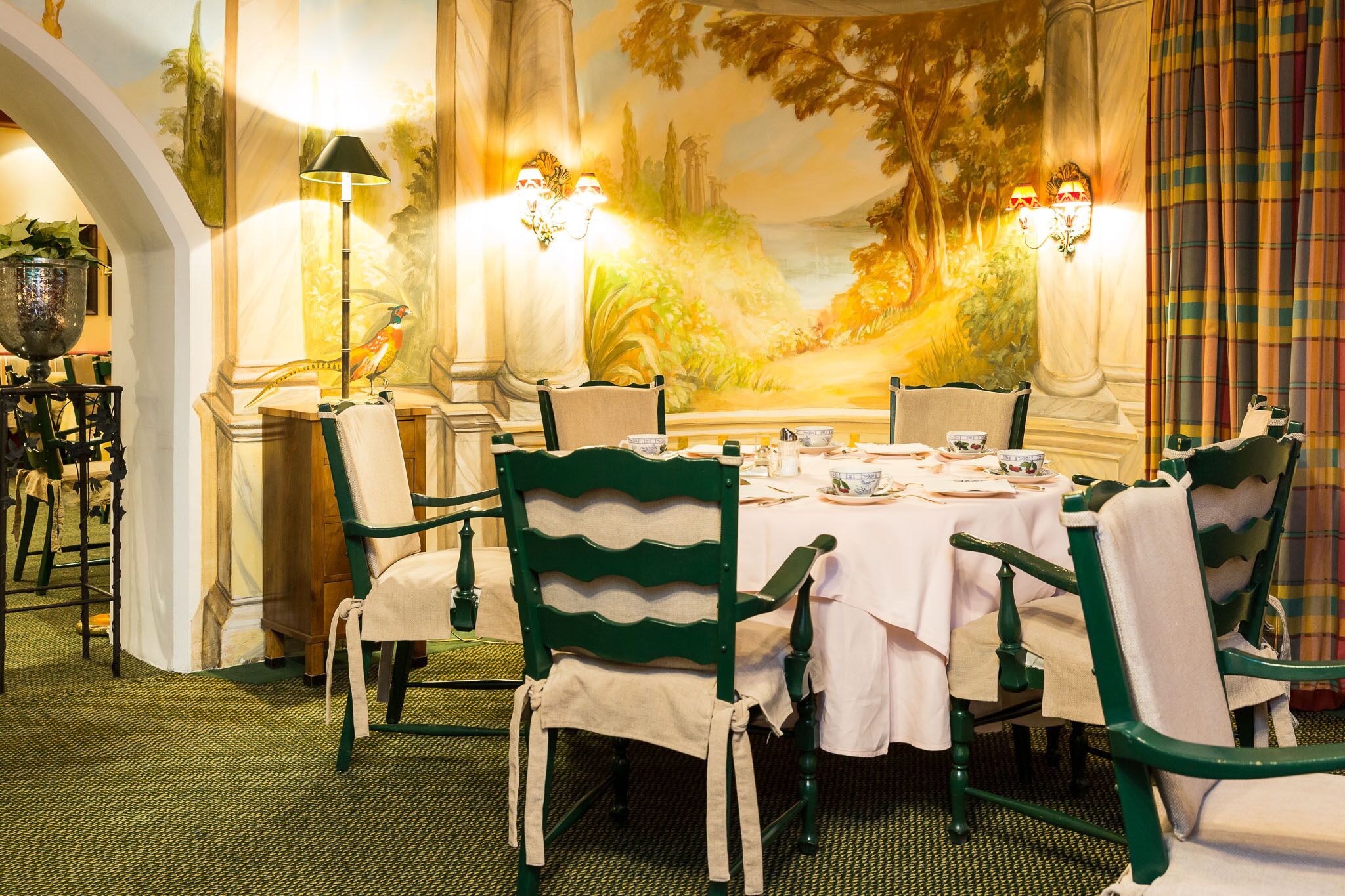 A dining area with a mural, green chairs, and a white tablecloth.