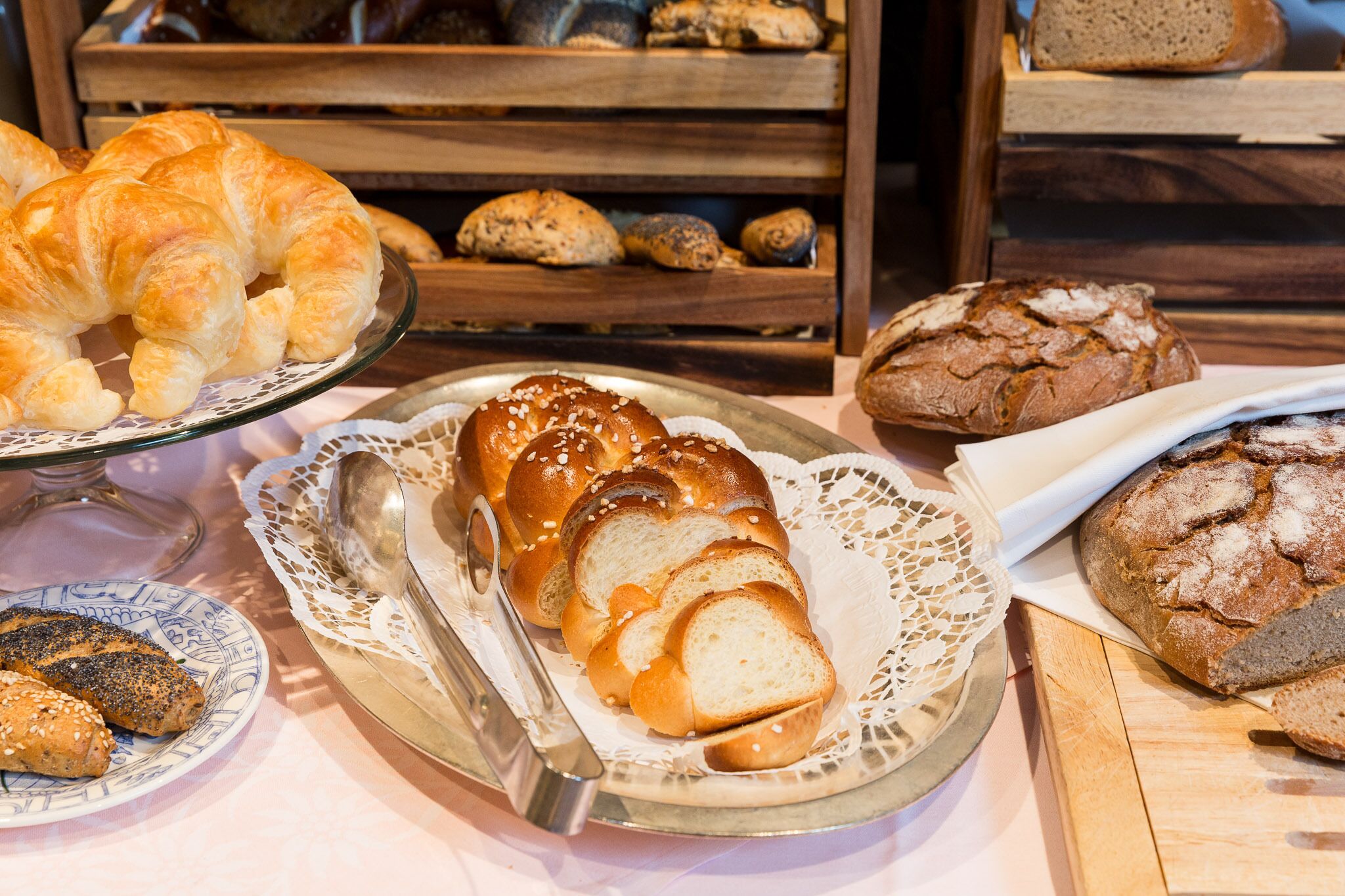 A variety of baked goods including croissants, bread, and rolls displayed on trays and plates.