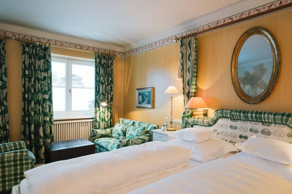 A hotel room with a large bed, a nightstand, a lamp, a window with curtains, and a mirror on the wall.