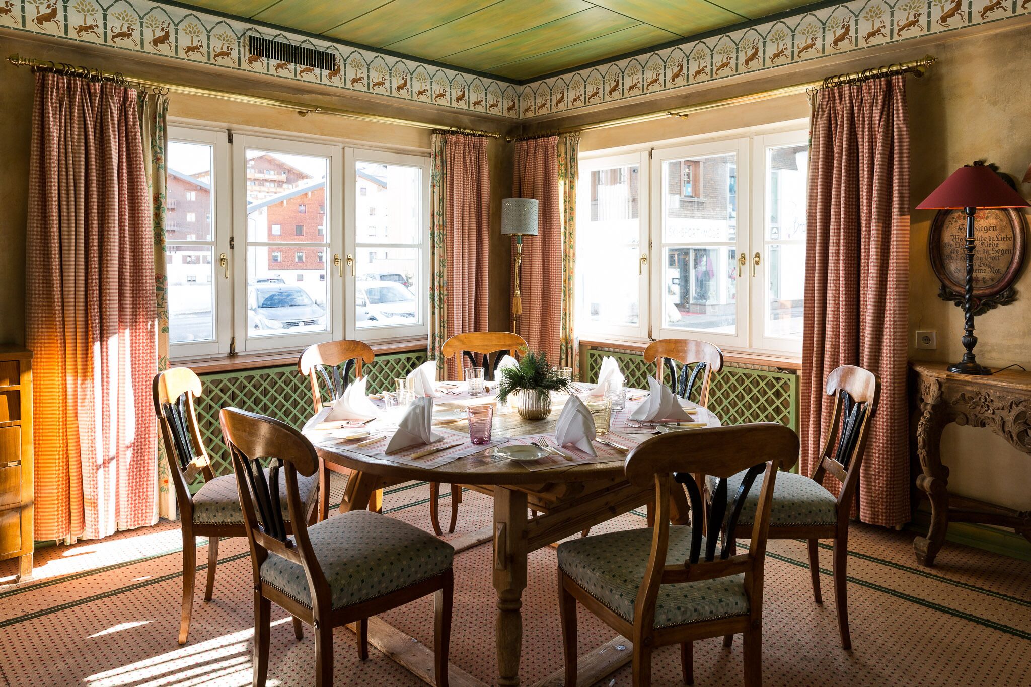 A dining area with a round table set for six, surrounded by wooden chairs with cushioned seats.