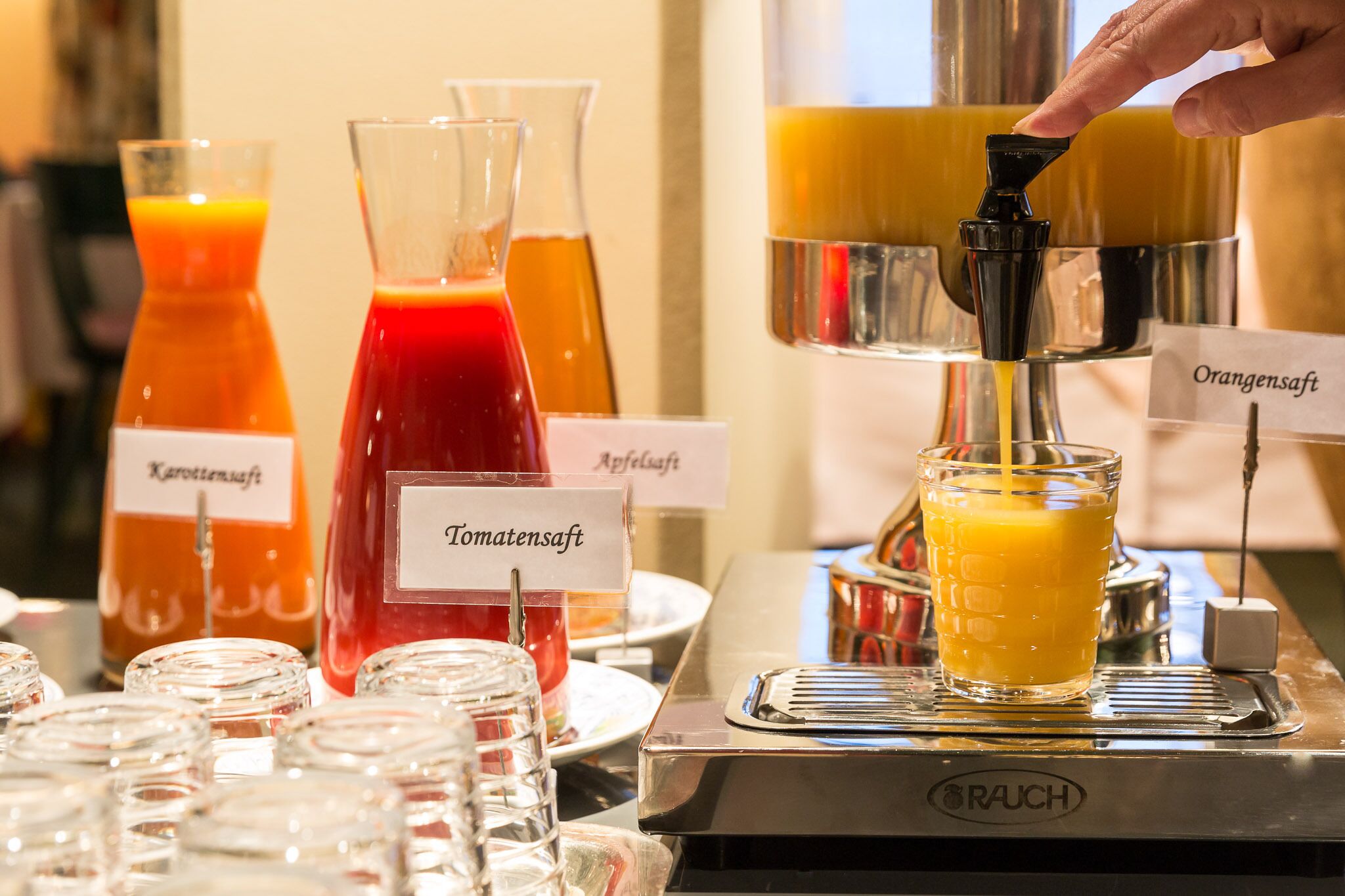 A beverage station with labeled dispensers for Karottensaft, Tomatensaft, Apfelsaft, and Orangensaft.