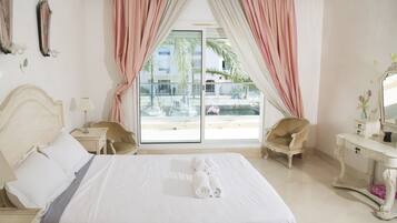Habitación de hotel con una cama grande, un tocador con espejo, una silla y vistas al exterior.