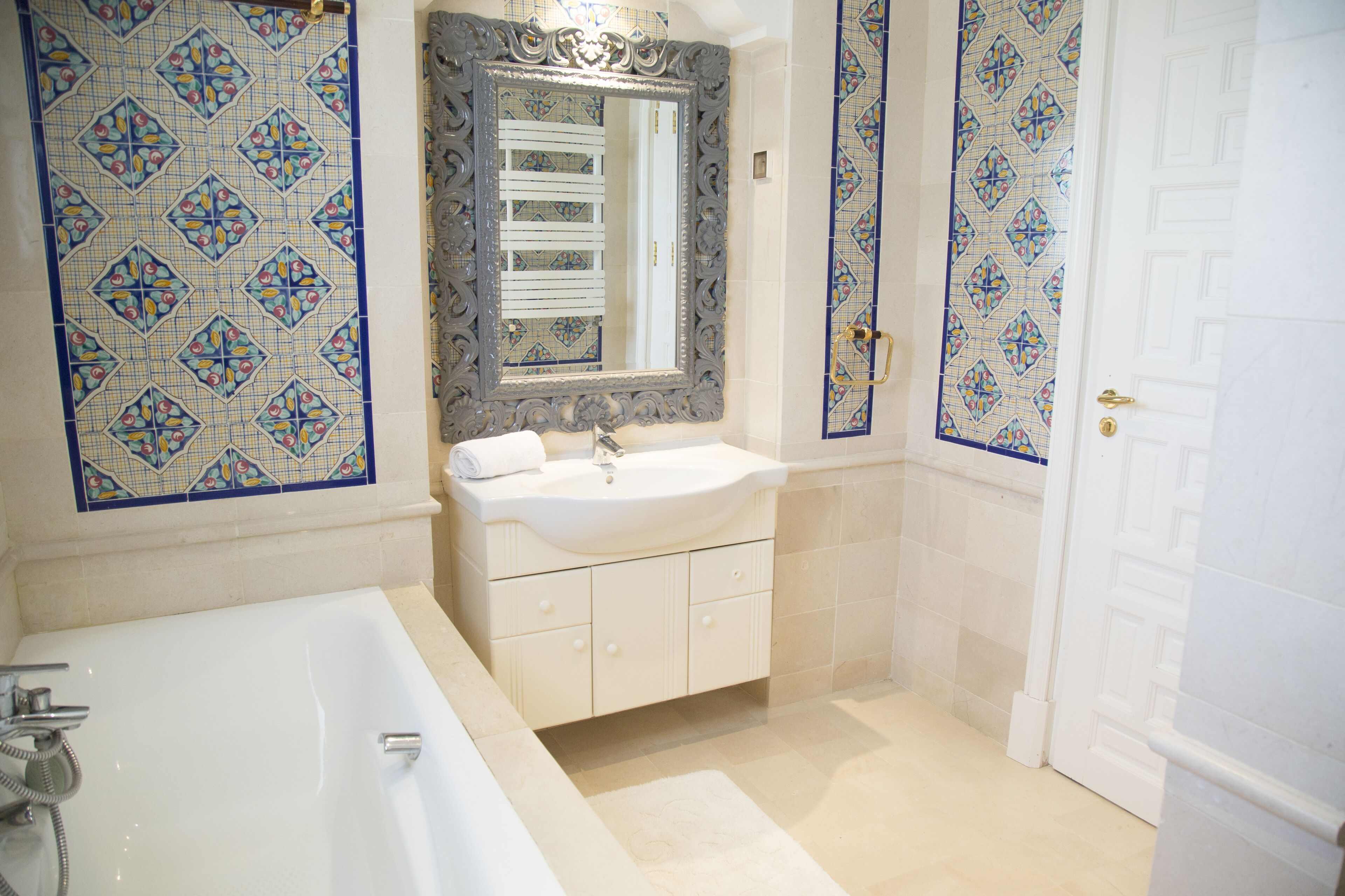 Ein Badezimmer mit einer weißen Badewanne, einem Waschbecken mit Spiegel darüber und blauen und weißen dekorativen Fliesen an den Wänden.