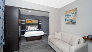 A modern hotel room with a bed, a sofa, a painting, and a wooden side table. - Days Inn by Wyndham Galt/Elk Grove South (Galt)