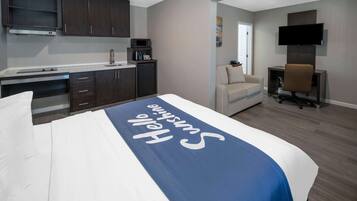A hotel room with a bed, a desk, a chair, a TV, and a kitchenette.