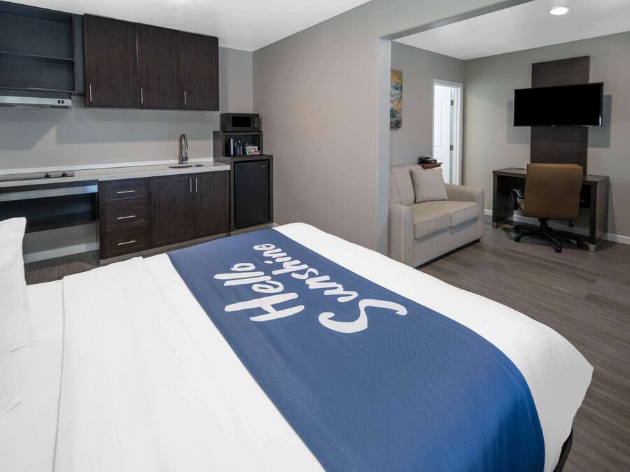 A hotel room with a bed, a desk, a chair, a TV, and a kitchenette.