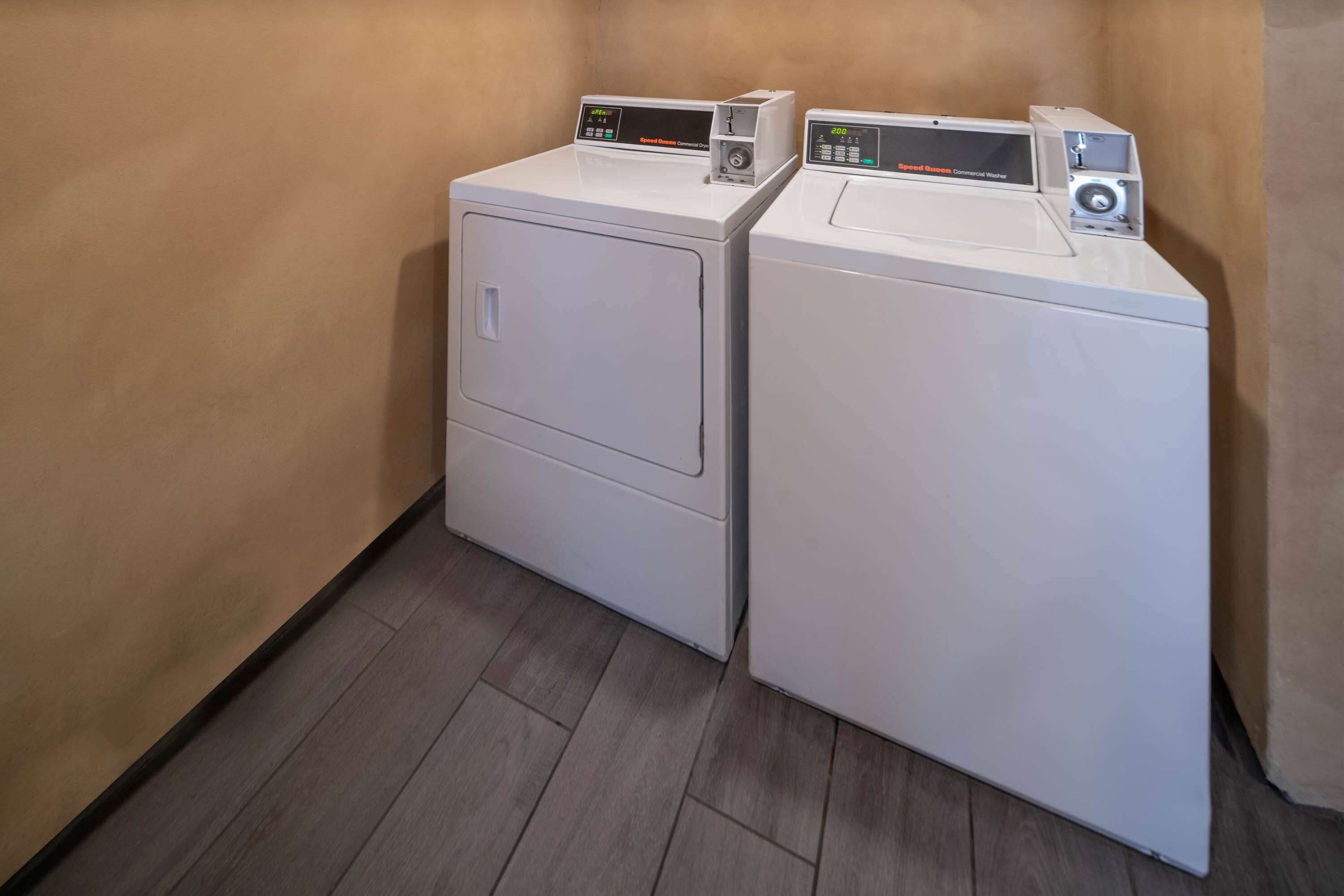 Two stacked front-loading washing machines in a laundry room with wooden flooring and beige walls.