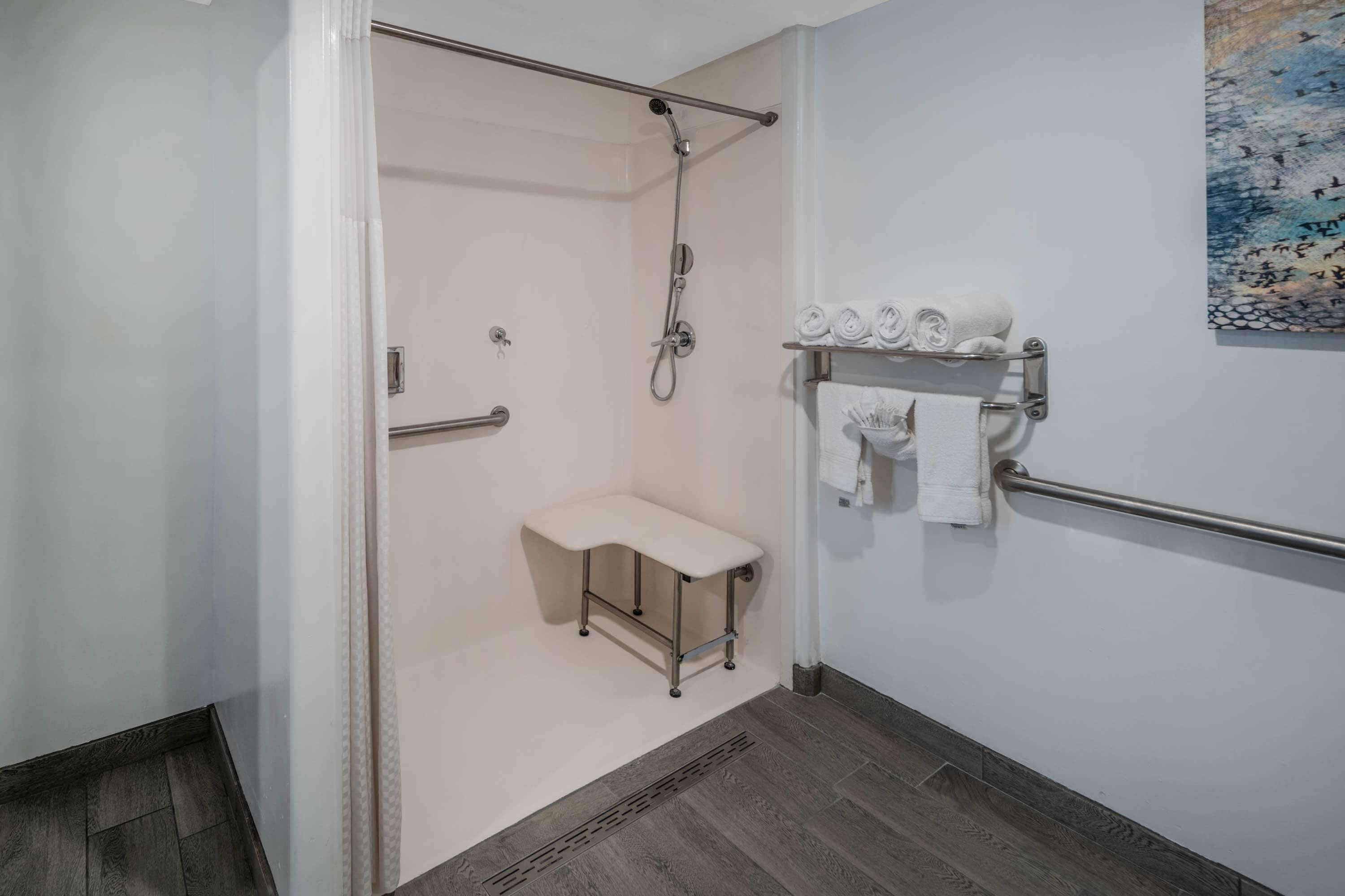 A modern bathroom with a shower, a bench, and a towel rack.