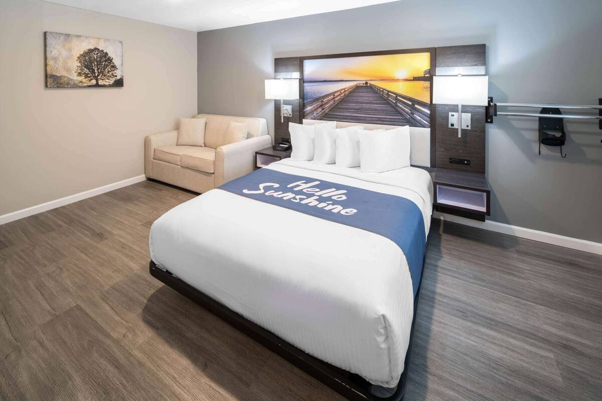 A hotel room with a bed, a chair, a painting, and a view of a pier.
