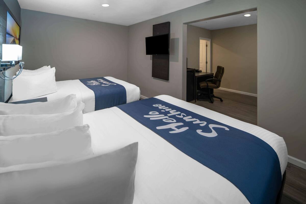 A hotel room with two beds, a desk, and a chair.