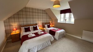 A bedroom with two beds, plaid wallpaper, a sloped ceiling, and a window with a view. - Kennedy Cottage - Newly Refurbished 3 Bedroom Cottage on Blairquhan estate (Maybole)