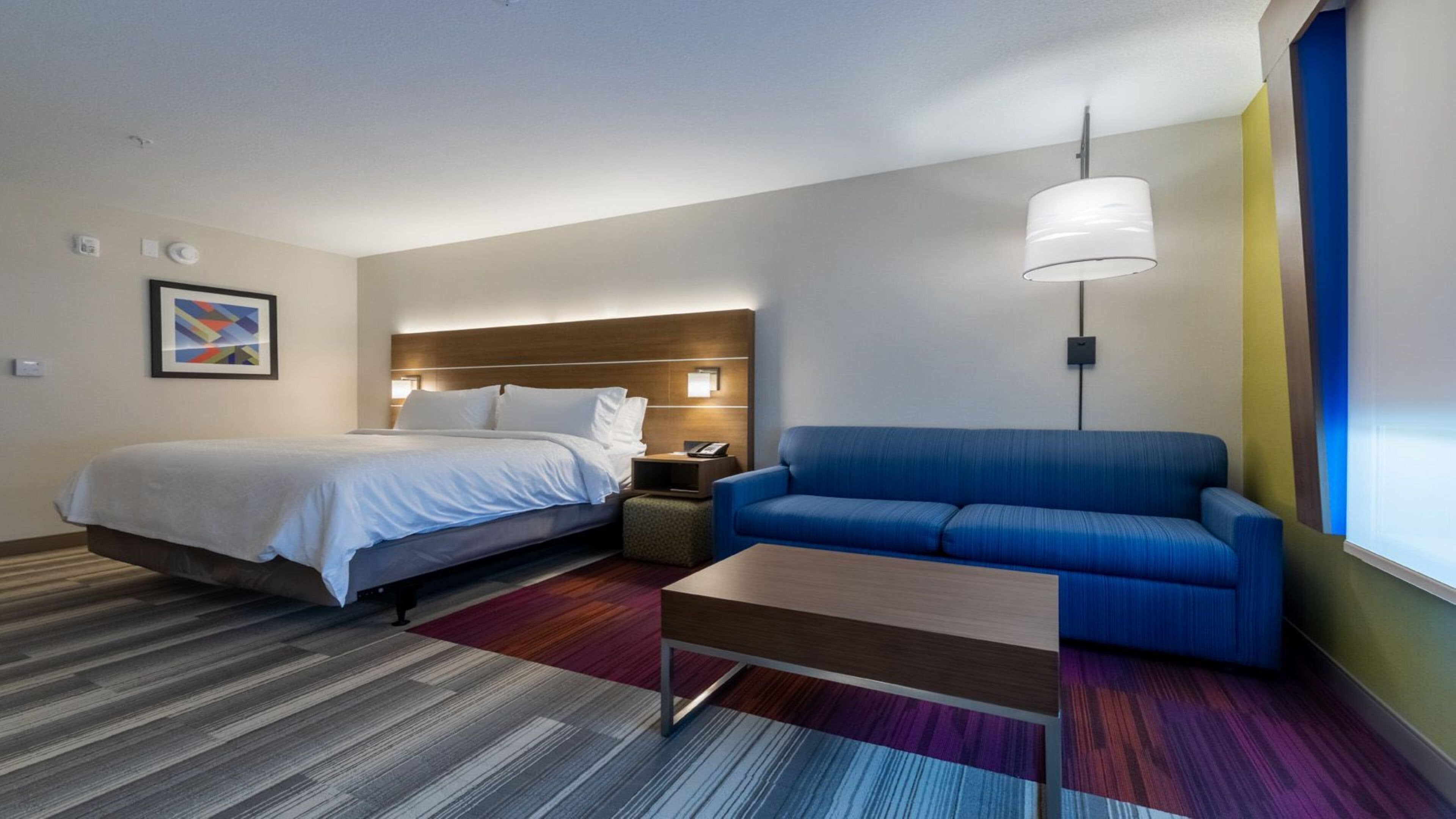 A hotel room with a bed, a blue sofa, a small table, and a colorful rug.