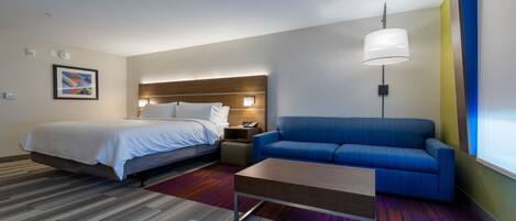 Habitación de hotel con una cama, un sofá azul, una mesita pequeña y una alfombra colorida.