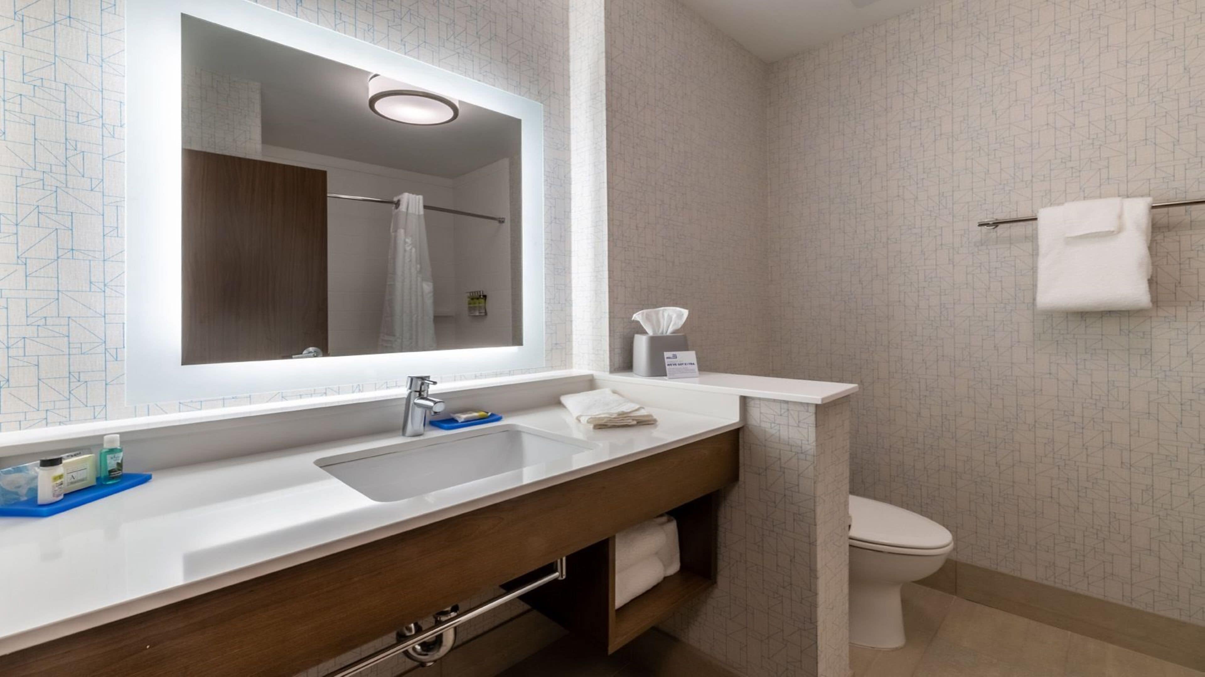 A modern bathroom with a large mirror, a sink, and a toilet.