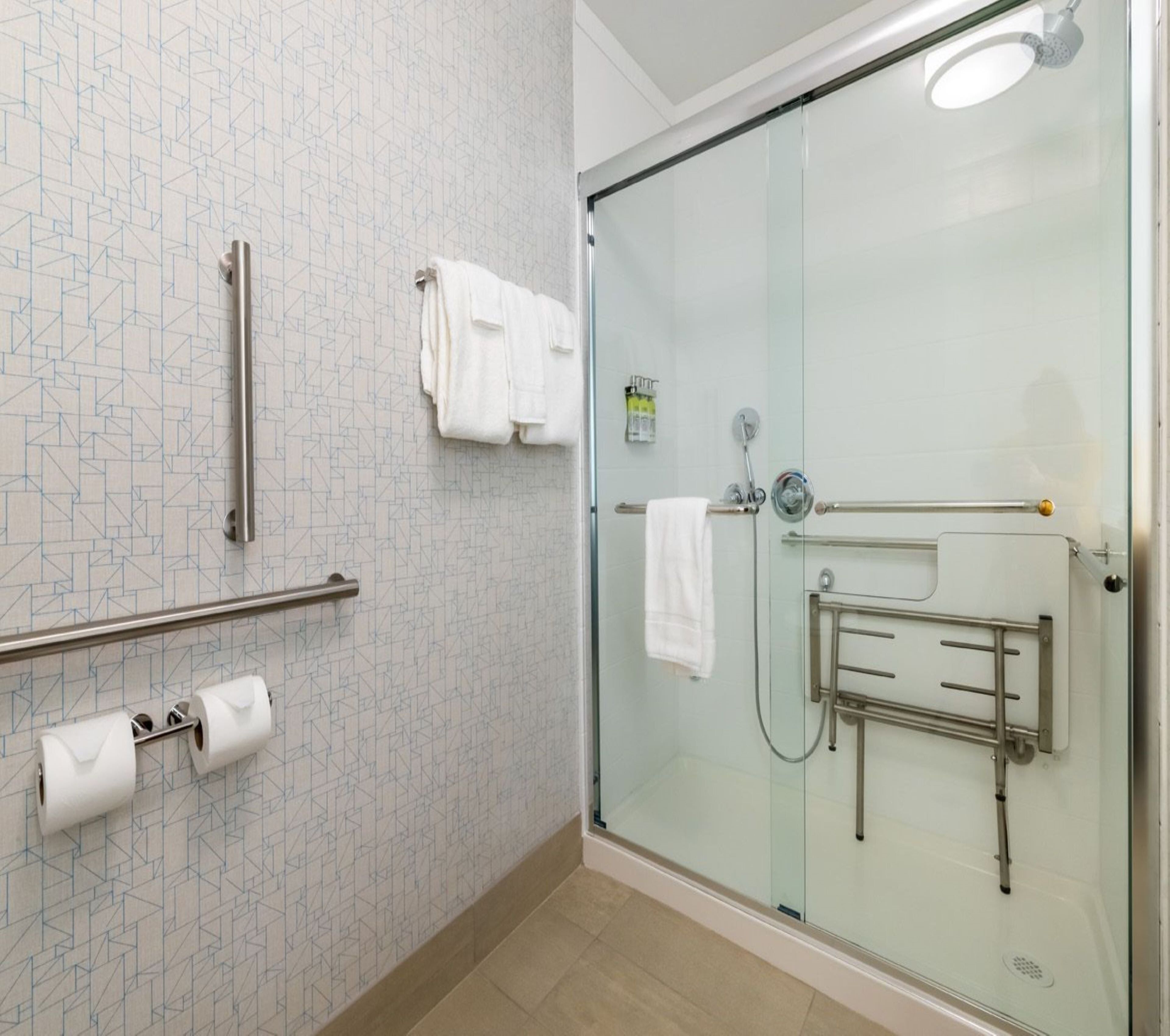 Un bagno moderno con box doccia in vetro, maniglione, porta asciugamani e porta carta igienica.
