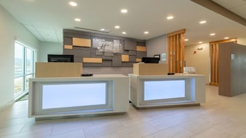 Zona de recepción con dos mostradores, un panel informativo en la pared y una puerta de madera.
