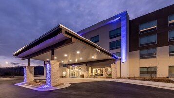 A modern hotel entrance with a covered waiting area, a stone pillar, and a well-lit facade.
