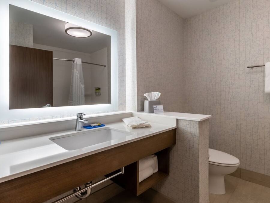 Ein modernes Badezimmer mit großem Spiegel, Waschbecken, Toilette und Handtuchhalter.