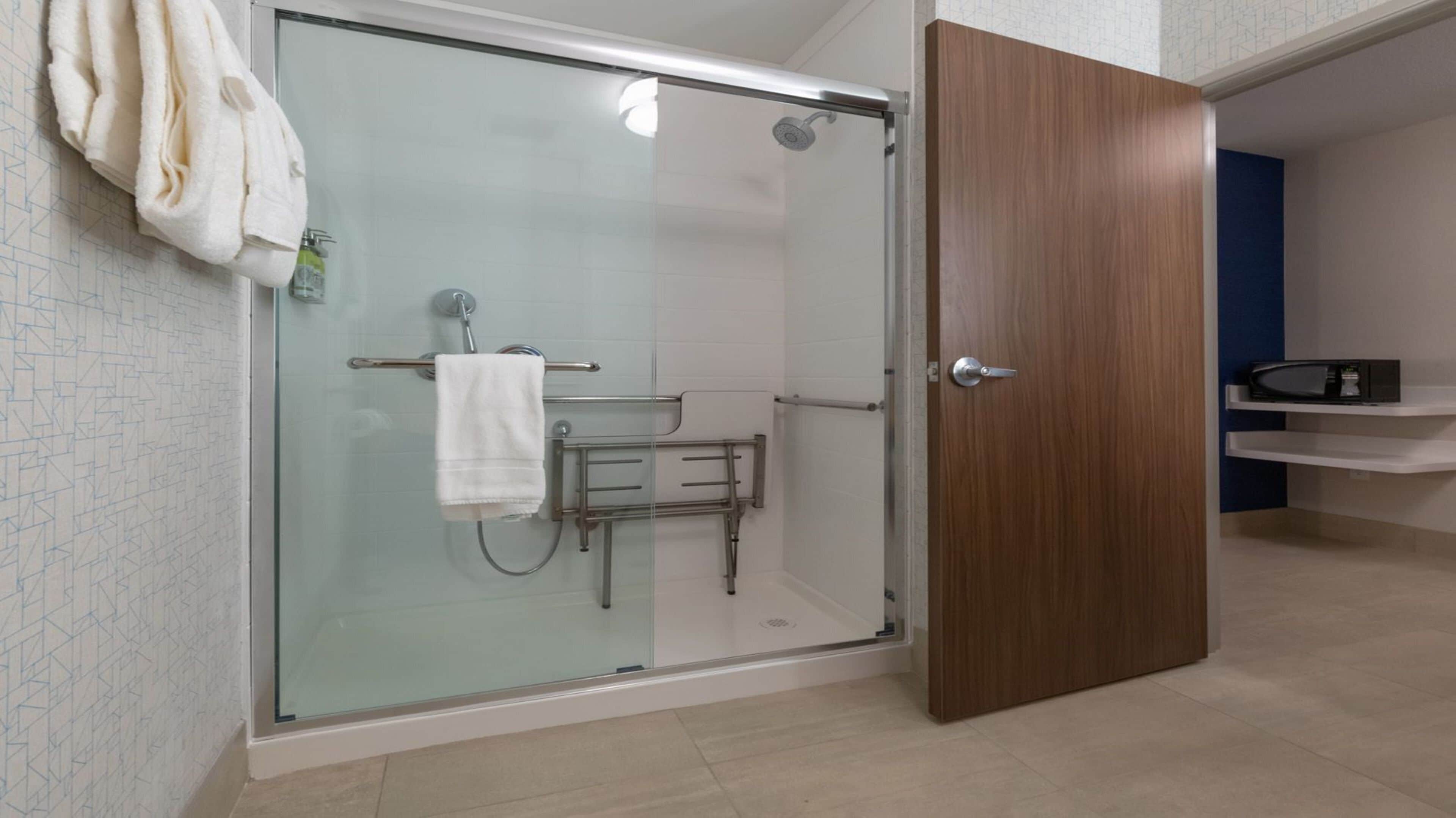 A glass-enclosed shower area with a towel rack, a handheld showerhead, and a grab bar.