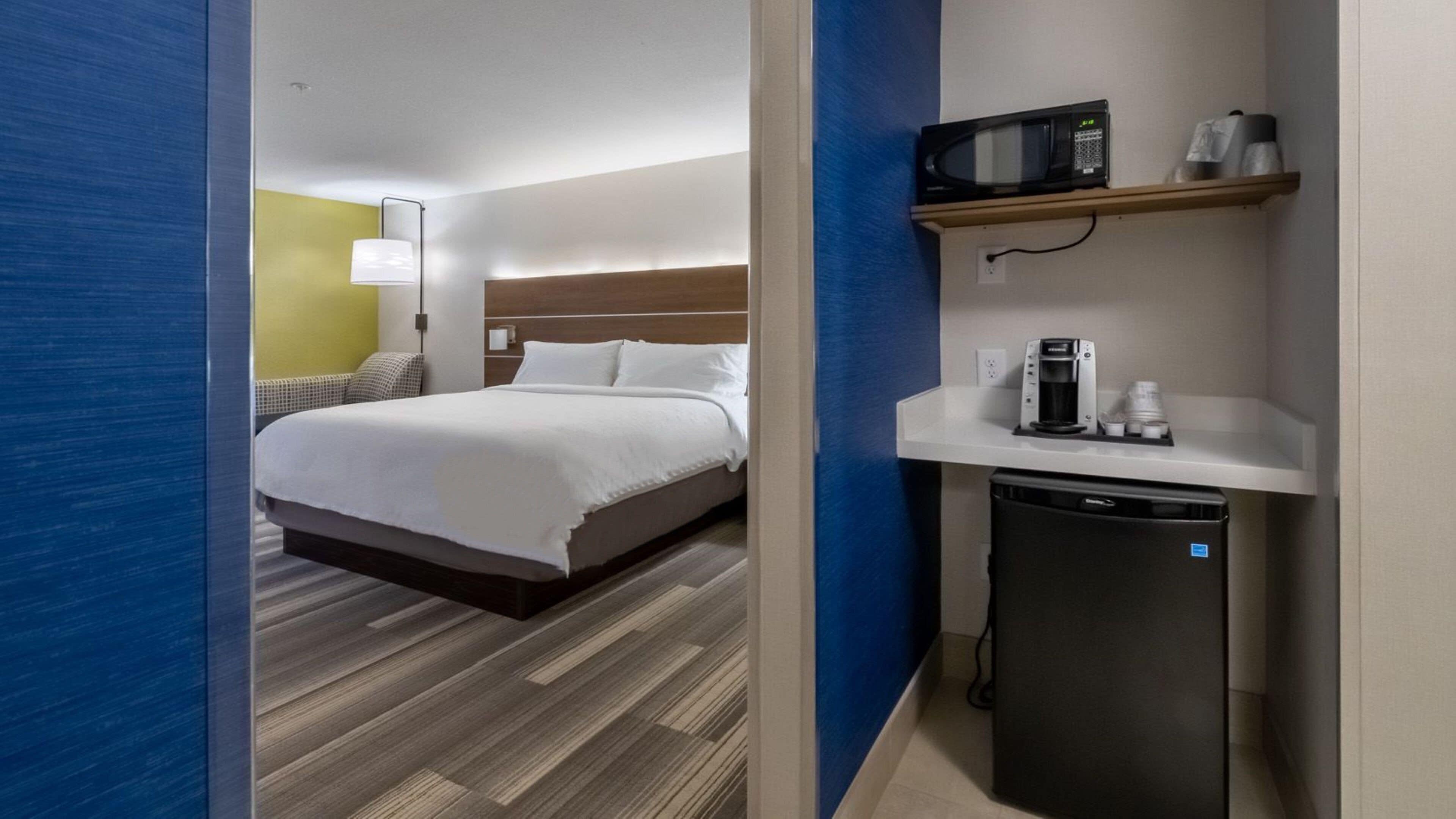 A hotel room with a bed, bedside table, microwave, and a small kitchenette area.