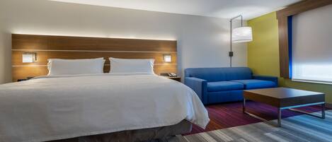 Una habitación de hotel con una cama grande, un sofá azul, una mesita pequeña y una mesita de noche con una lámpara.