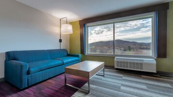 A modern room with a blue sofa, a wooden coffee table, and a large window with a view of a city and mountains.