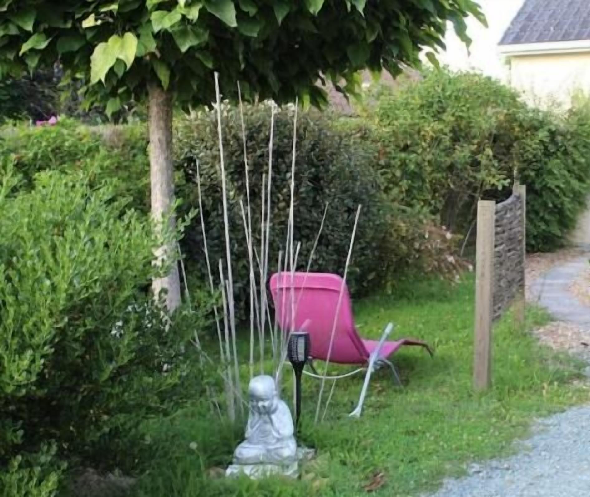 A garden with a statue, a pink chair, and a stone wall.