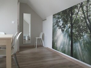 Une pièce moderne décorée d’une grande fresque représentant une forêt, avec une table à manger en bois et des chaises blanches.