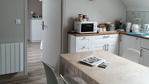 A modern kitchen with white cabinets, a microwave, and a clock on the wall. There is a dining table with chairs and a magazine on it. - Chambre et Appartement Zen de Beauval (Seigy)