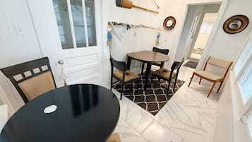 Un comedor con una mesa redonda y sillas, una puerta blanca con ventana, y una red de pesca colgada en la pared.