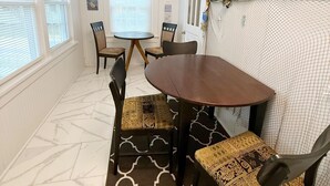 A dining area with a round table, chairs, a patterned rug, and a window with blinds. - Updated home 2 blocks from water in Colonial Beach-come visit Driftwood Cottage! (Colonial Beach)