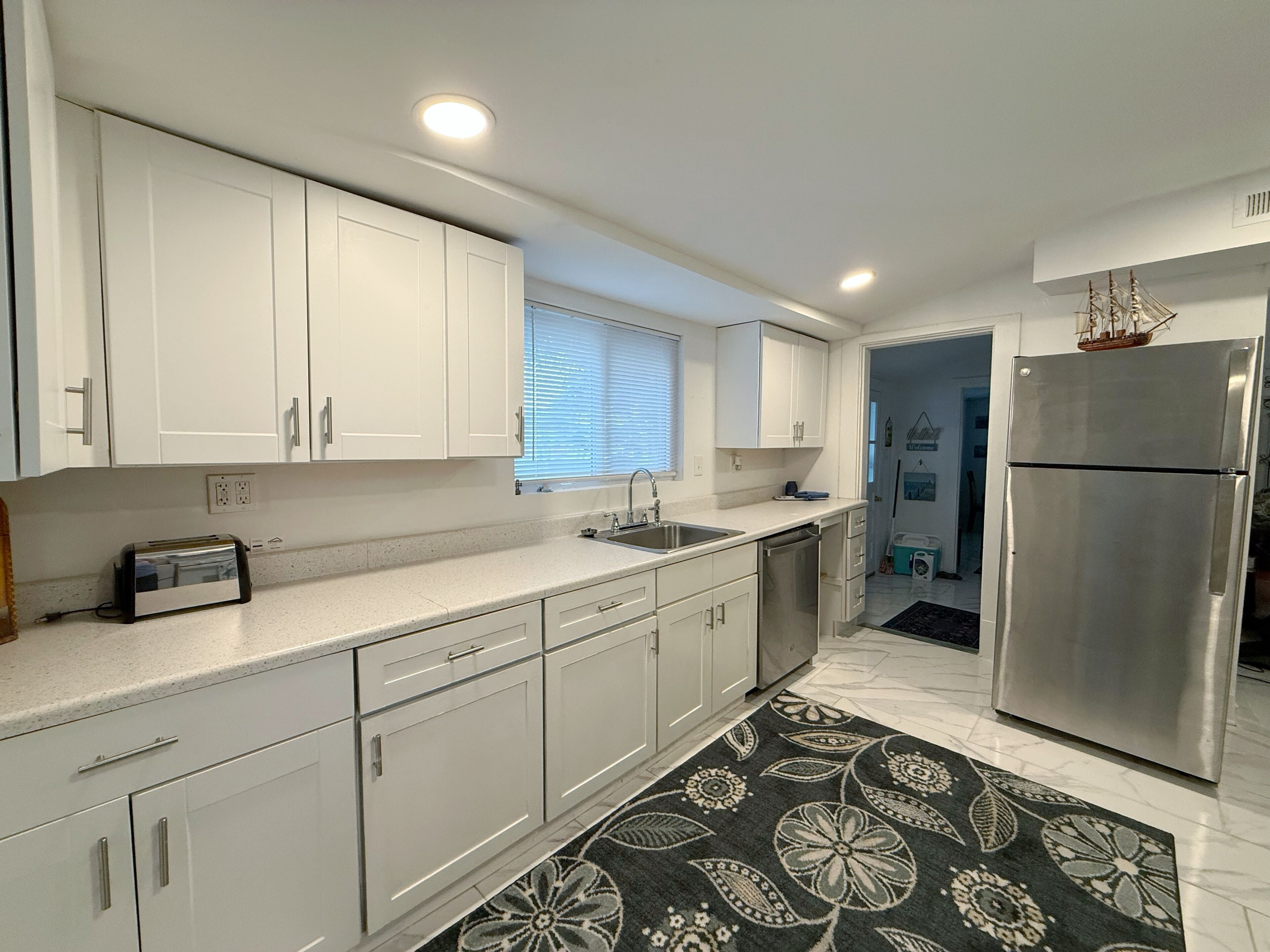 Una cocina moderna con armarios blancos, un refrigerador de acero inoxidable y una alfombra estampada.