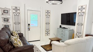 A living room with a brown leather sofa, a white sofa, a glass coffee table, a small wooden side table, a television, and decorative metal panels on the walls. - Updated home 2 blocks from water in Colonial Beach-come visit Driftwood Cottage! (Colonial Beach)