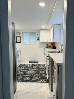 Una cocina estrecha con armarios blancos, piso de mármol y alfombra estampada.