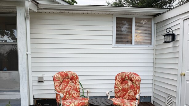 A patio with two chairs and a table, a window with blinds, and a door with a lantern. - Updated home 2 blocks from water in Colonial Beach-come visit Driftwood Cottage! (Colonial Beach)