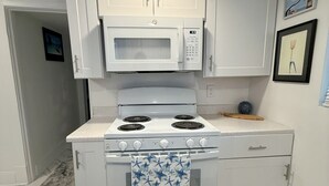 A compact kitchen with white cabinets, a microwave, a stove, and a patterned rug. - Updated home 2 blocks from water in Colonial Beach-come visit Driftwood Cottage! (Colonial Beach)