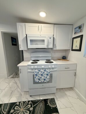 Una cocina compacta con armarios blancos, microondas, estufa y una alfombra estampada.