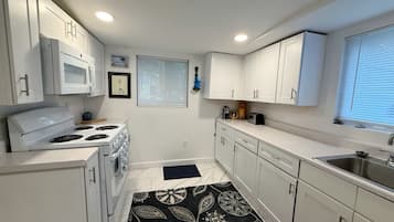 Una cocina compacta con armarios blancos, estufa, microondas y pileta.