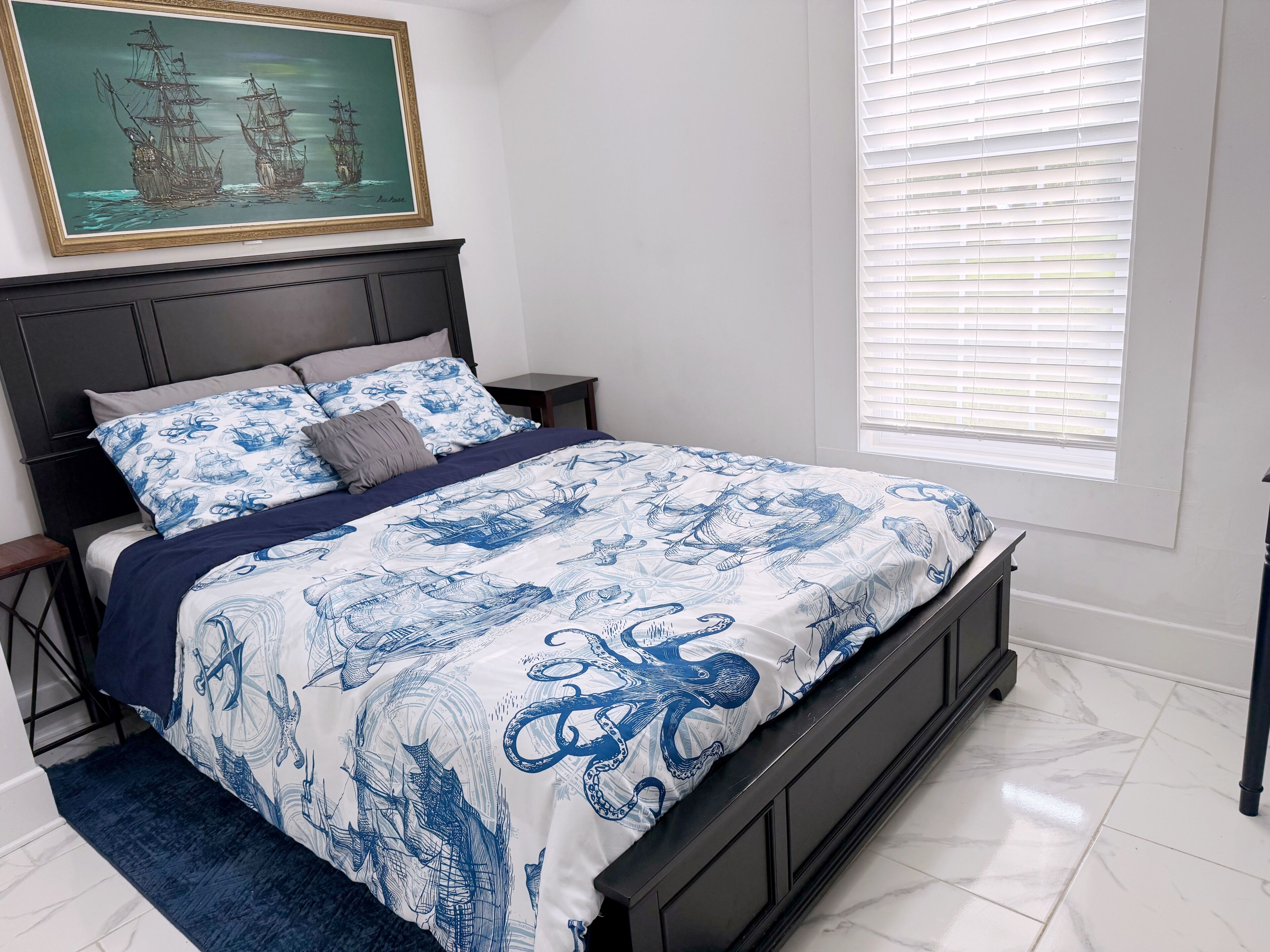 Un dormitorio con una cama, una mesita de noche, una ventana con persianas y un cuadro en la pared.