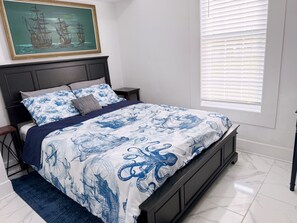 Un dormitorio con una cama, una mesita de noche, una ventana con persianas y un cuadro en la pared.