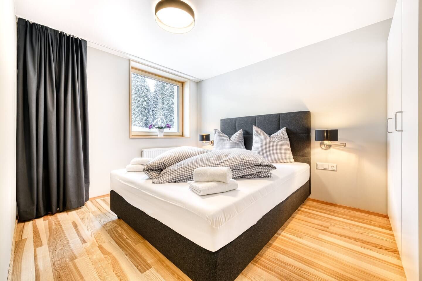 Une chambre moderne avec un grand lit, une fenêtre donnant sur des arbres couverts de neige et un plancher en bois.